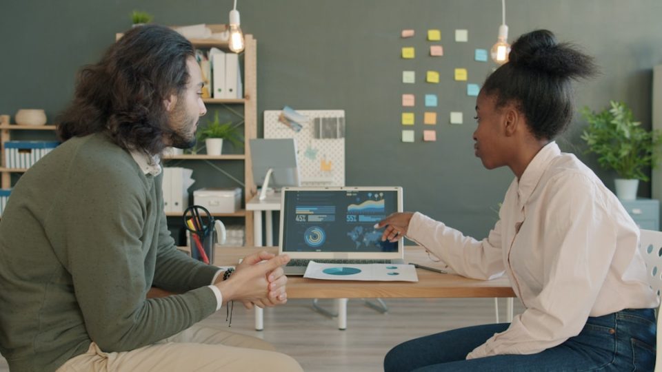 Two colleagues discussing data on a laptop screen. business team analyzing qr code analytics dashboard, data charts on screen, marketing performance graphs