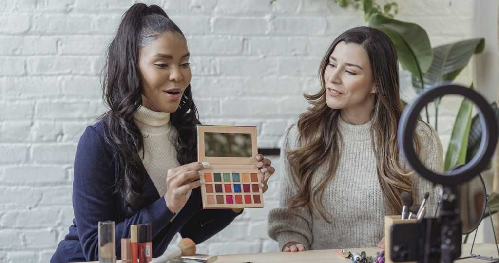 Young diverse ladies recording vlog about makeup products on smartphone