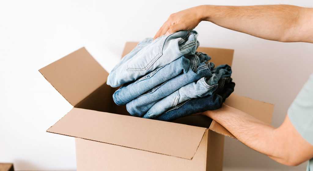 Crop man packing casual clothes into carton box