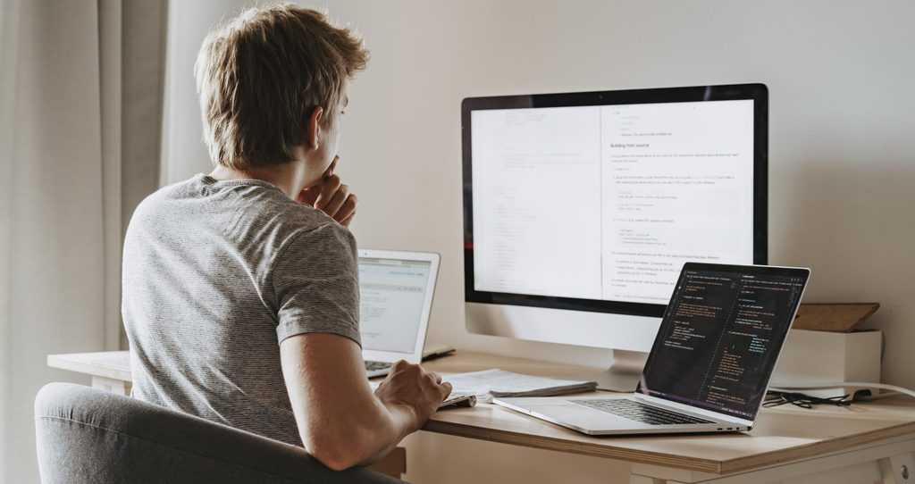 Man sitting in front of three computers