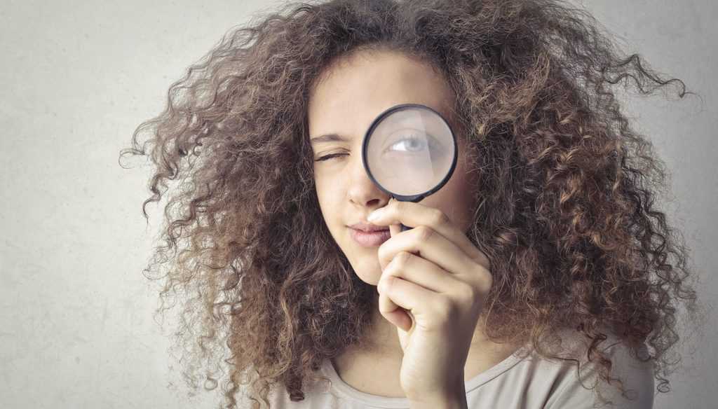 Portrait photo of woman holding up a magnifying glass over her eye