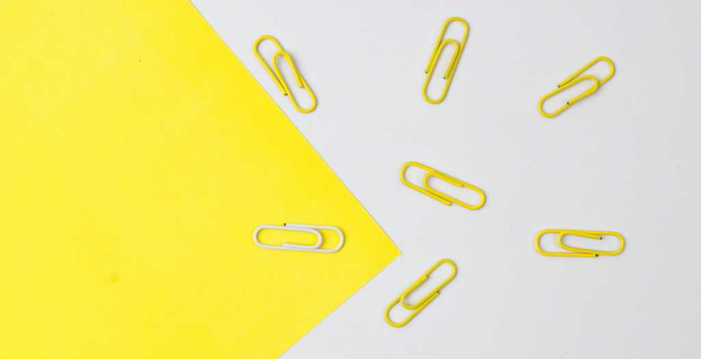 Yellow color paper clips with only a white one isolated on paper background