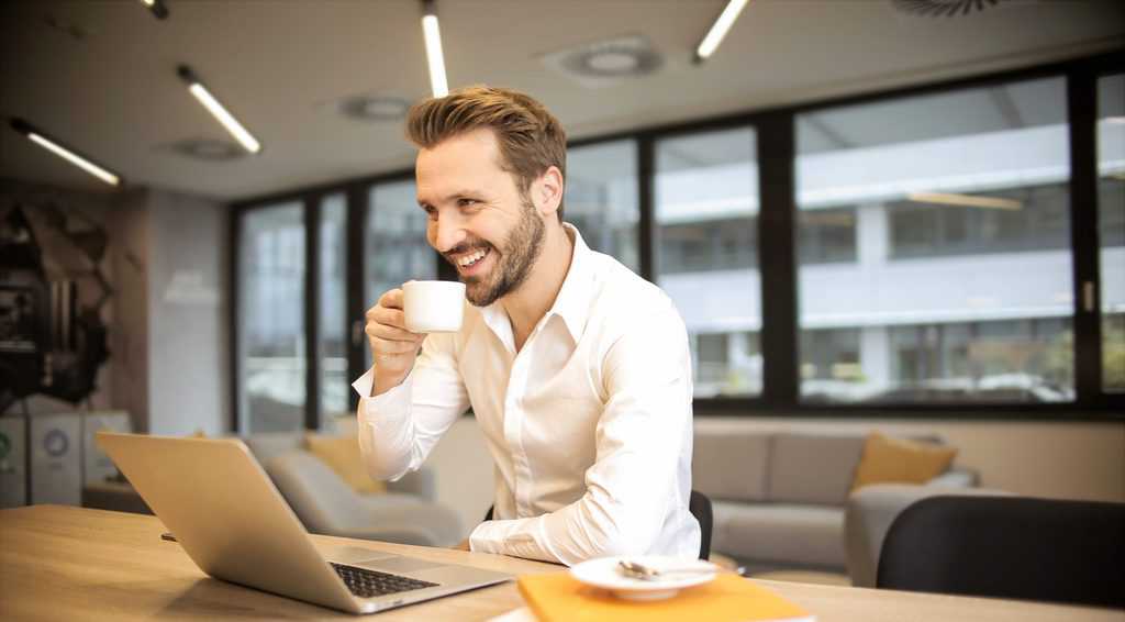 Depth of field photo of man sitting on chair while holding cup in front of table