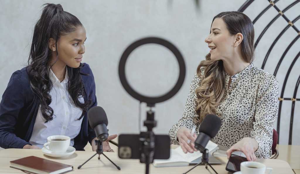 Smiling woman interviewing black female guest and recording video