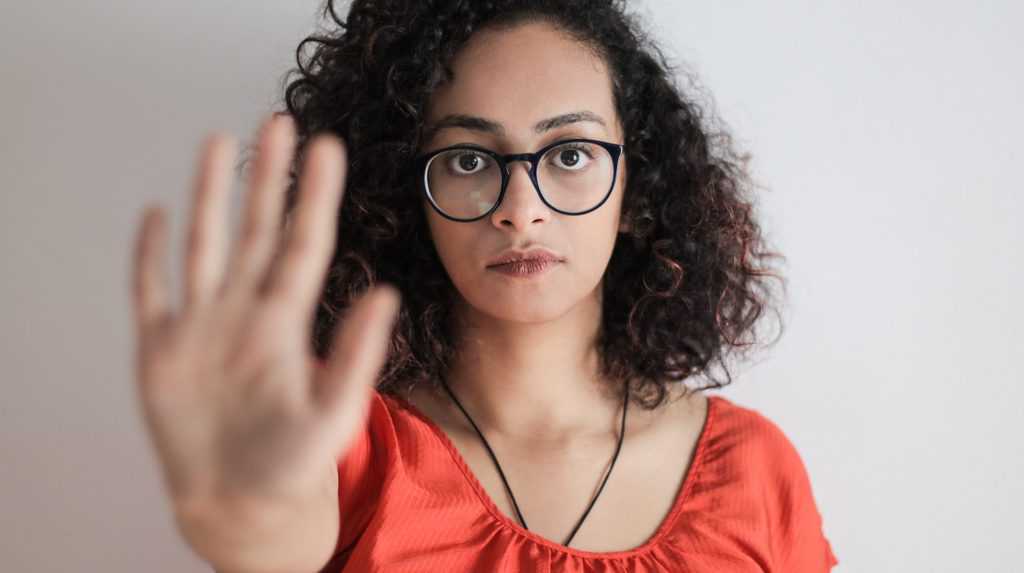 Portrait photo of woman in red top wearing black framed eyeglasses holding out her hand in stop gesture