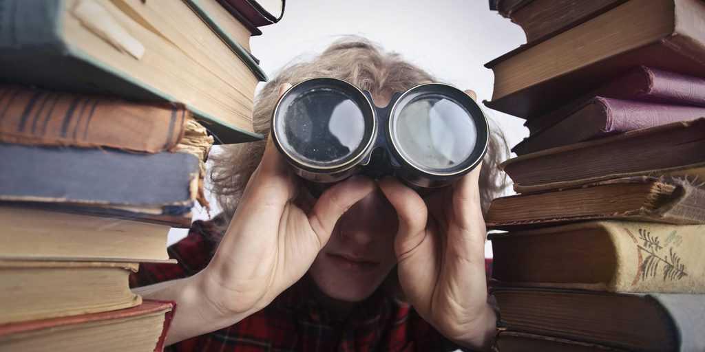 Man using binoculars in between stack of books