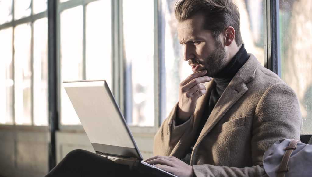 Man wearing brown jacket and using grey laptop