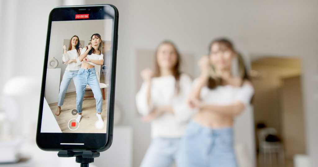 Woman in white sleeveless shirt and blue denim skirt holding black smartphone