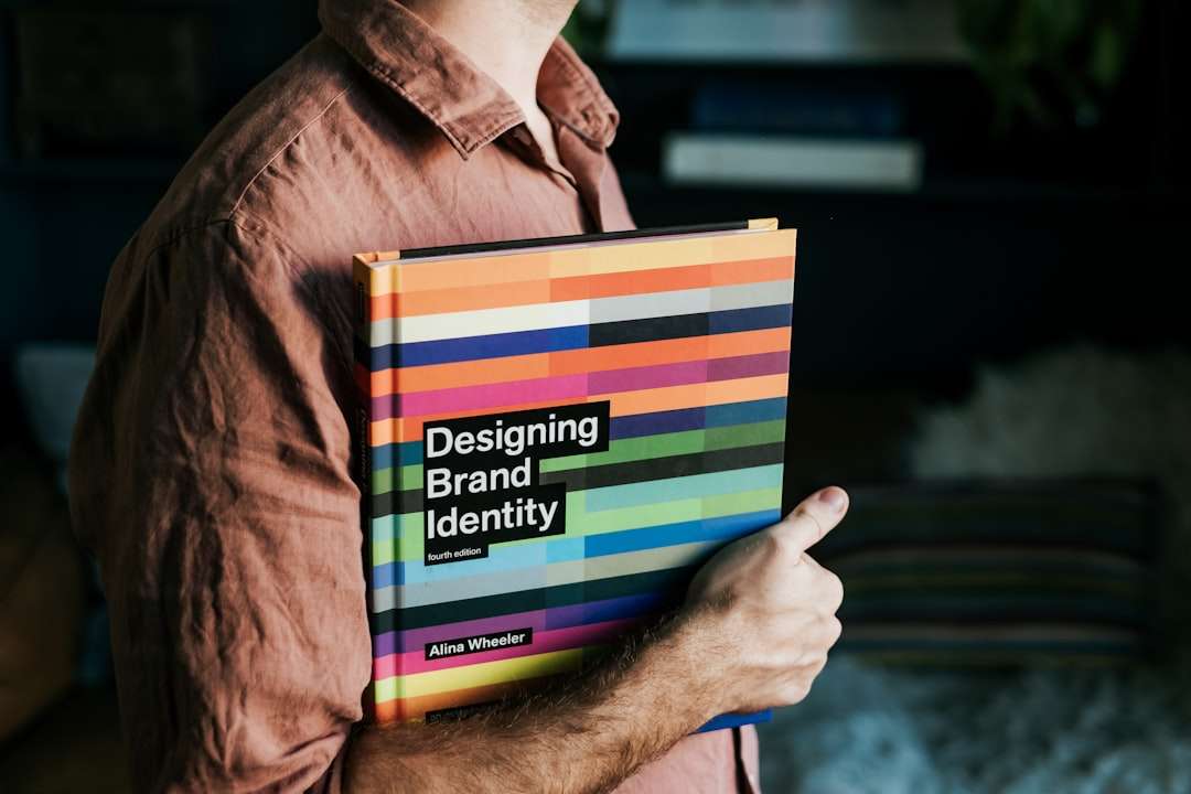 a man holding a book that says designing brand identity brand consistency, logos, marketing collateral