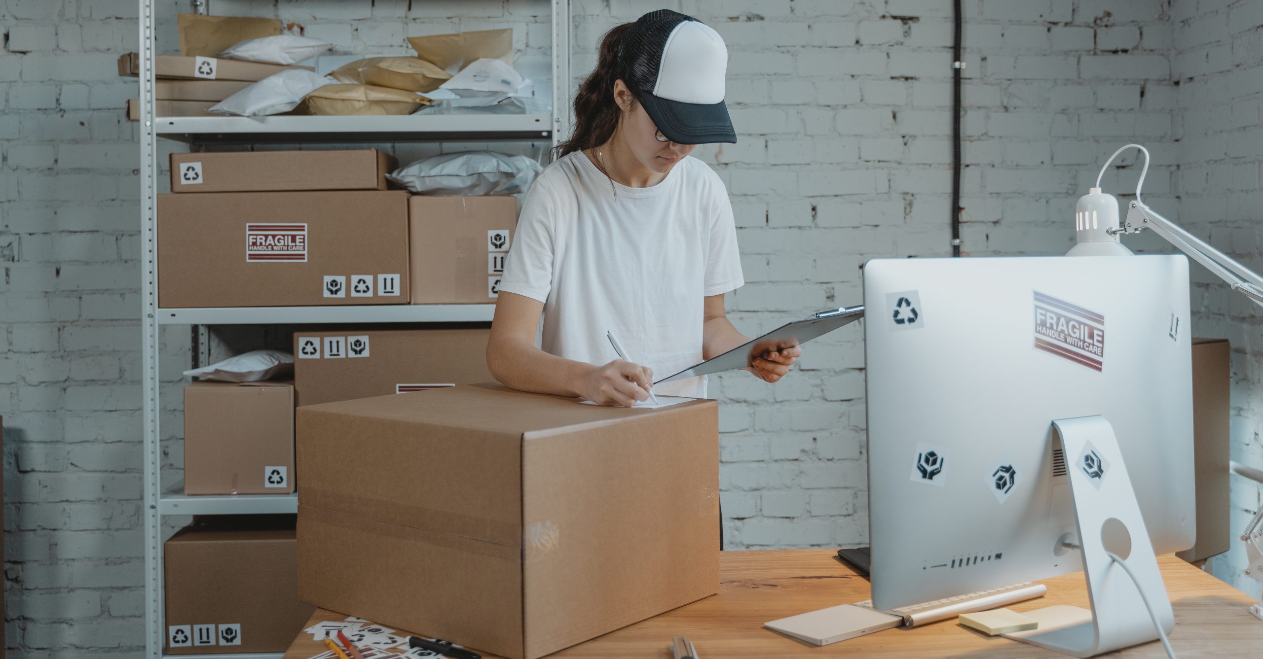 Woman writing down on a carton box while looking at a clipboard