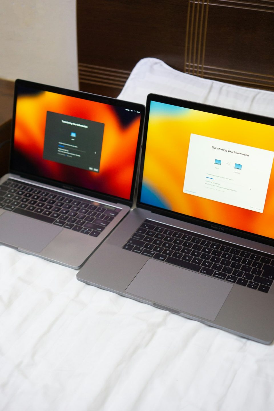 a couple of laptops sitting on top of a bed mac laptop sharing internet, smart tv connection