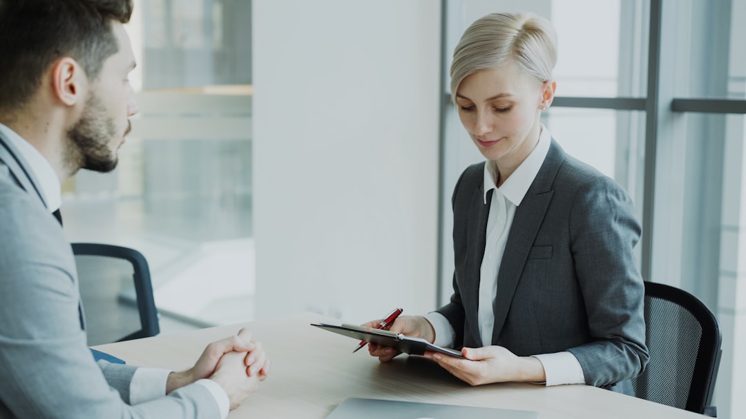Woman in suit reviews document with man. business contract signing, digital notarization screen, compliance documents, corporate office meeting