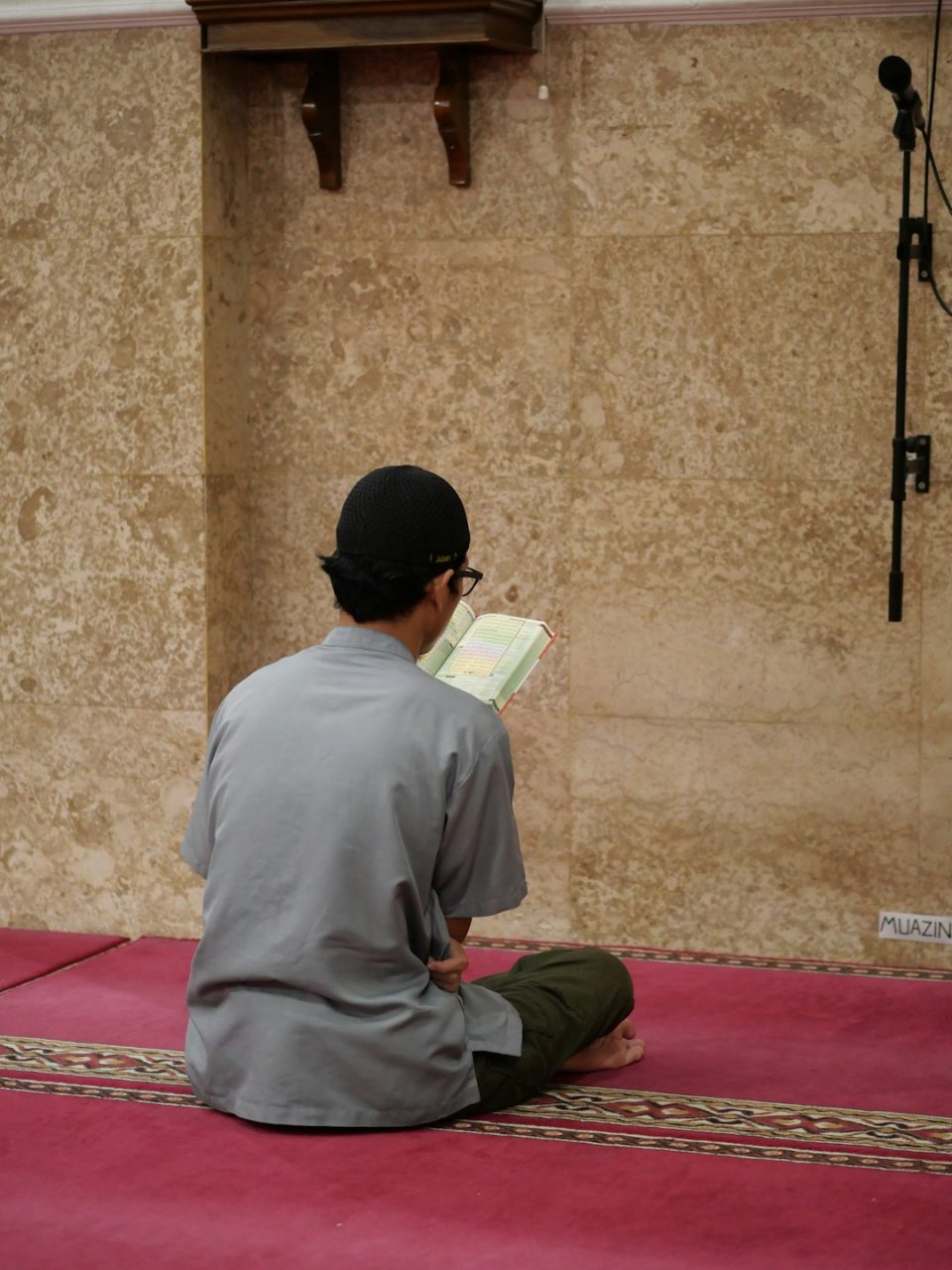 a man sitting on the floor reading a book quran, manzil, digital reading