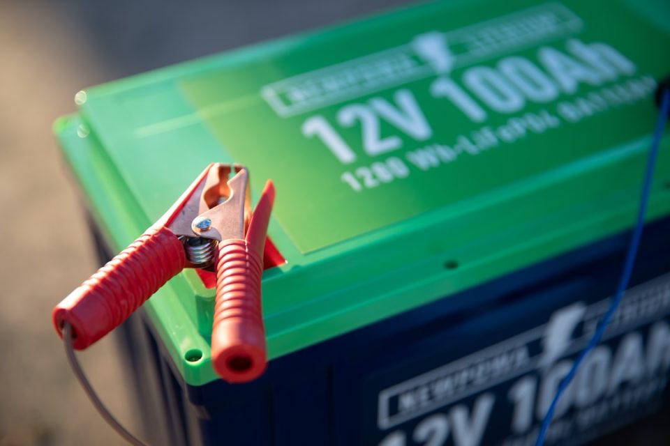 a red and green battery with a pair of pliers attached to it generator battery, generac maintenance, multimeter voltage check
