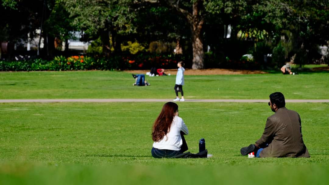 a couple of people sitting on top of a lush green field international students, australian university, campus life