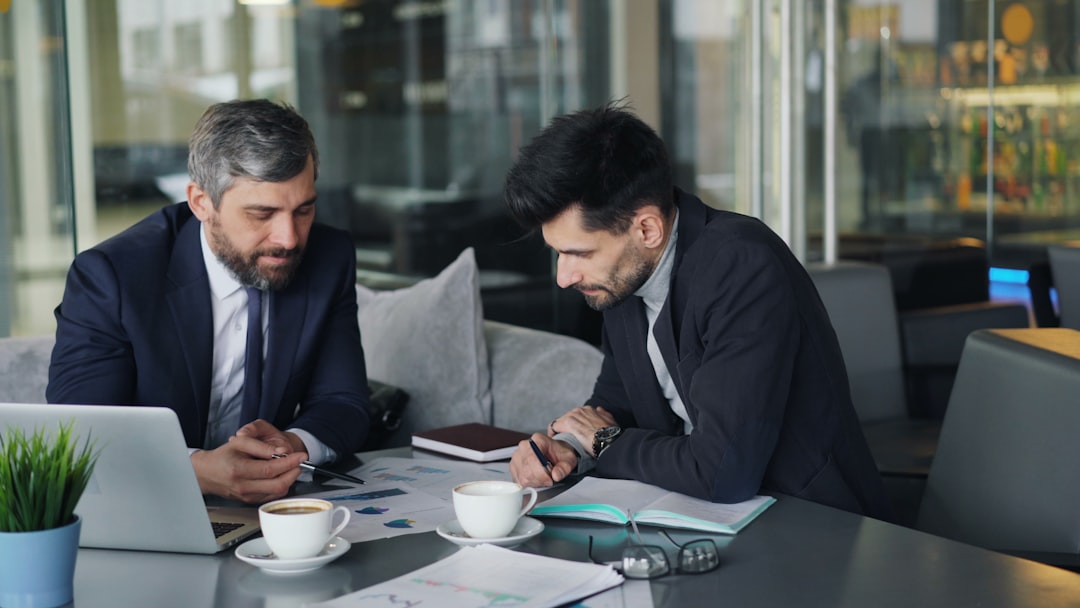 two men sitting at a table working on a laptop digital asset management dashboard interface, organized media library, business team reviewing assets